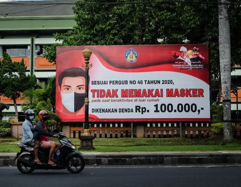 locals in Bali on motorbike infront of Masks covid sign