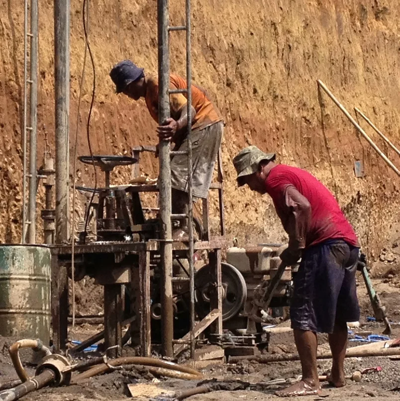 Horizontal closeup photo of two men working in a dug out area of land on a building construction site with machinery in a street in Ubud, Bali on a sunny day in Summer.