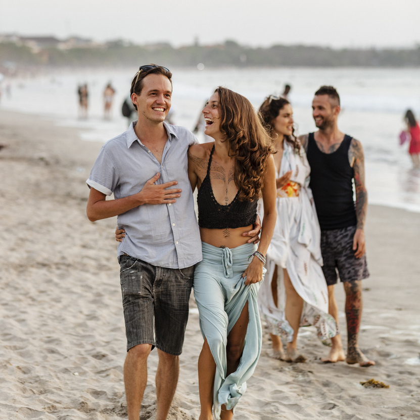 Two couples walking down Kuta beach in Bali, Indonesia while embracing and laughing with each other. The main focus is the couple at the front.