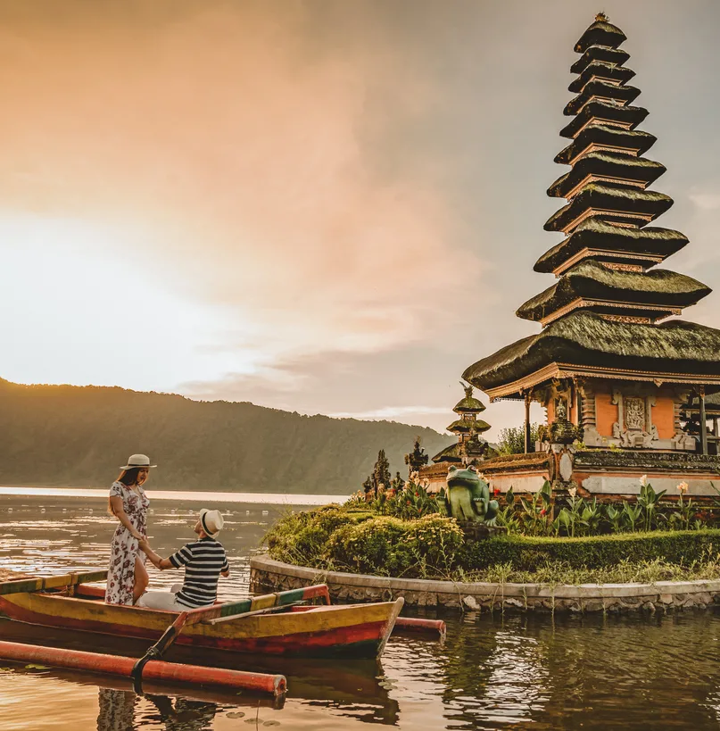 Happy romantic couple in love relaxing on honeymoon. The Ulun Danu Tamblingan Temple is located in the north side of Bali, in a Tamblingan lake . Tourist couple enjoying the lake. Photo of couple on a boat in the lake at sunset.