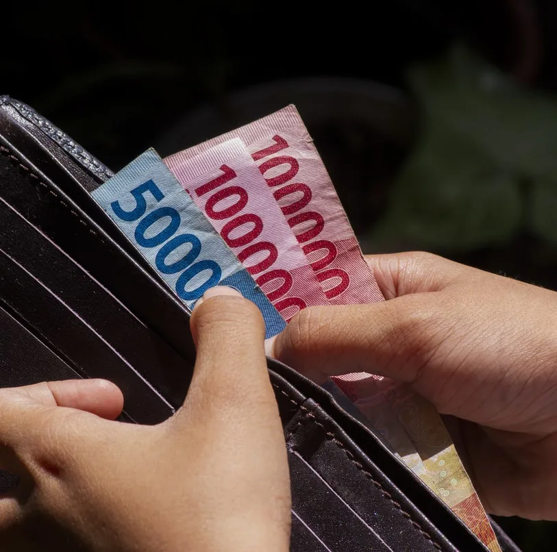 IDR cash notes being pulled from a black leather wallet