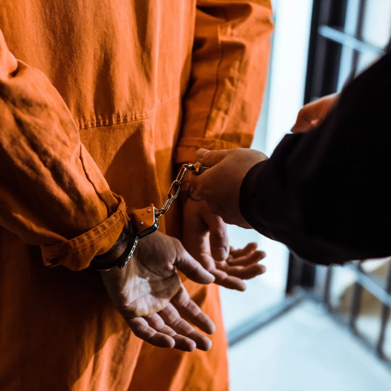 Close-Up-Of-Prison-Inmate-In-Orange-Overalls-With-Hands-In-Handcuffs