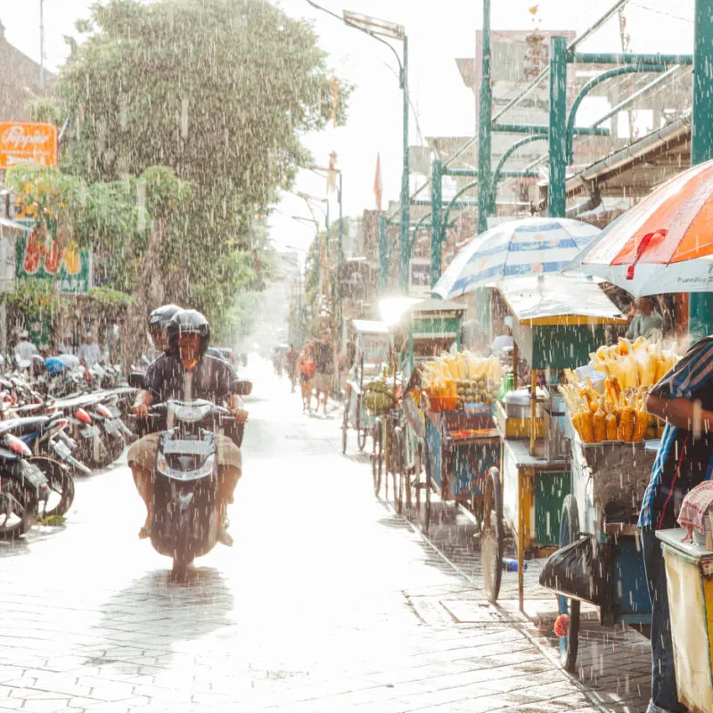 People-Drive-A-Moped-Down-A-Quiet-Street-In-Bali-Rain