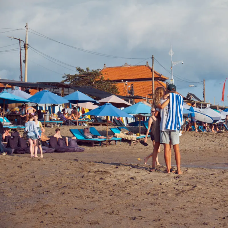 Tourists Enjoy Berawa Beach In Canggu Bali Beneath Blue Sun Umbrellas