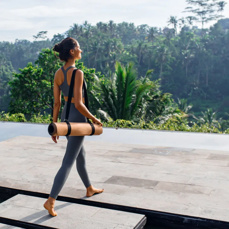 Woman-Carries-A-Yoga-Mat-Onto-Deck-Overlooking-Bali-Jungle