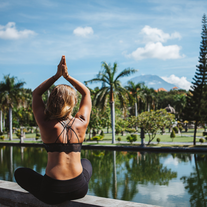 Woman-In-Yoga-Clothes-Sits-In-Prayer-Position-Next-To-Lake-In-Bali