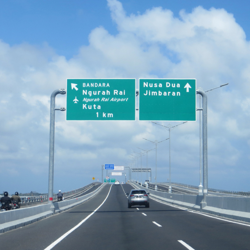 Car-Drives-Along-A-Quiet-Bali-Toll-Road-Under-Signs-To-Kuta-And-Nusa-Dua