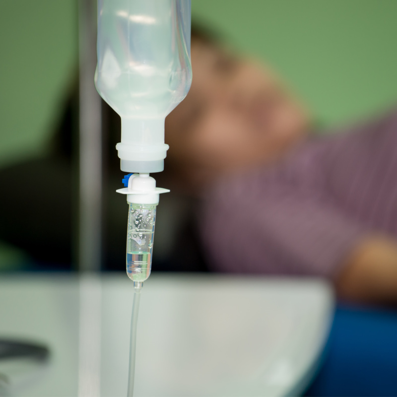 Close-Up-Of-IV-Drip-In-Hospital-With-Blurred-Patient-in-Background