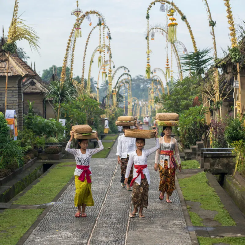 Women and Children In Bali Carry Baskets On Their Heads As They Walk To Village Temple