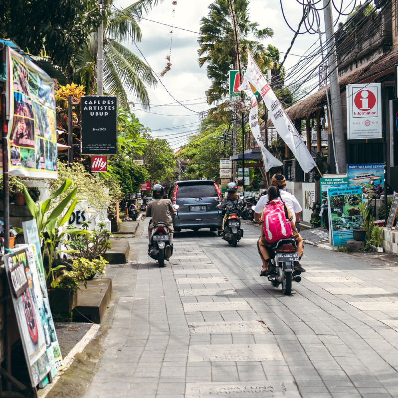 Moped-and-Car-Drivers-Drive-Through-Quiet-Bali-Street