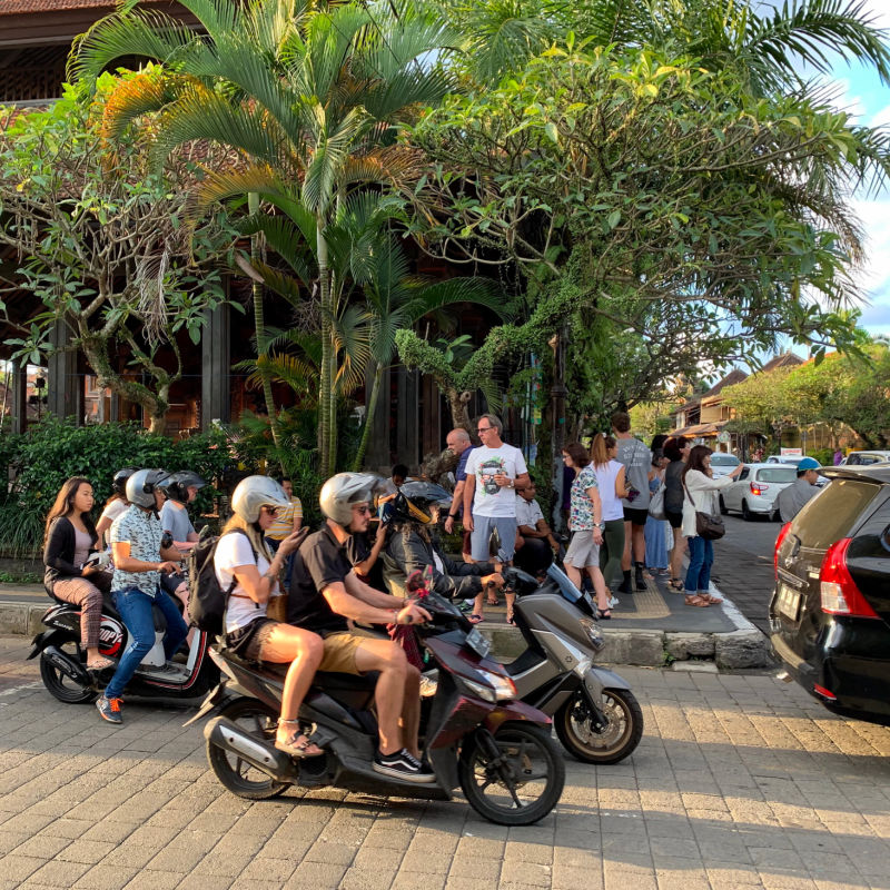 Tourists-Wait-At-Road-Crossing-In-Bali-Driving-Moped-Scooters