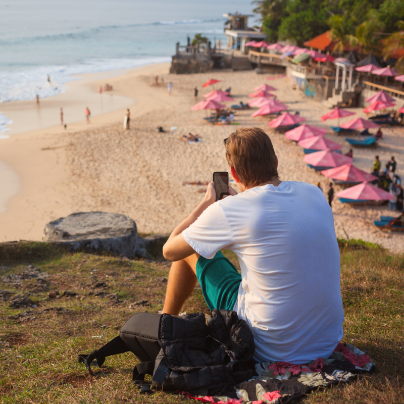 Traveler-Looks-Over-Bali-Beach-With-Phone-In-His-Hand