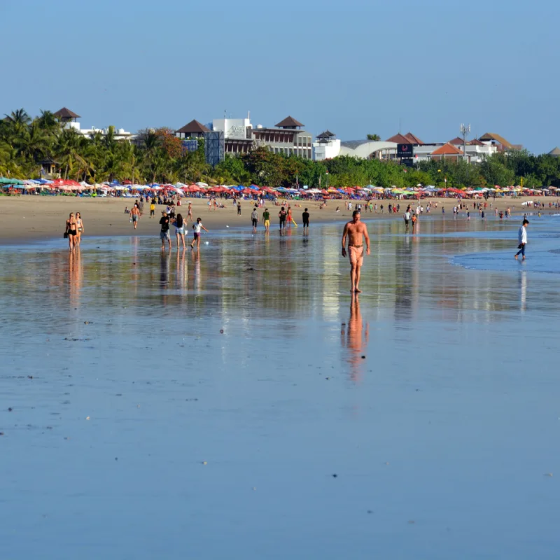 View Of Kuta Beach With Tourists Enjoying Sand and Shallow Ocean Water
