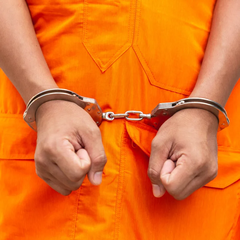 Close-Up-Of-Hands-In-Handcuffs-And-Prisoner-Is-Wearing-Bright-Orange-Overalls