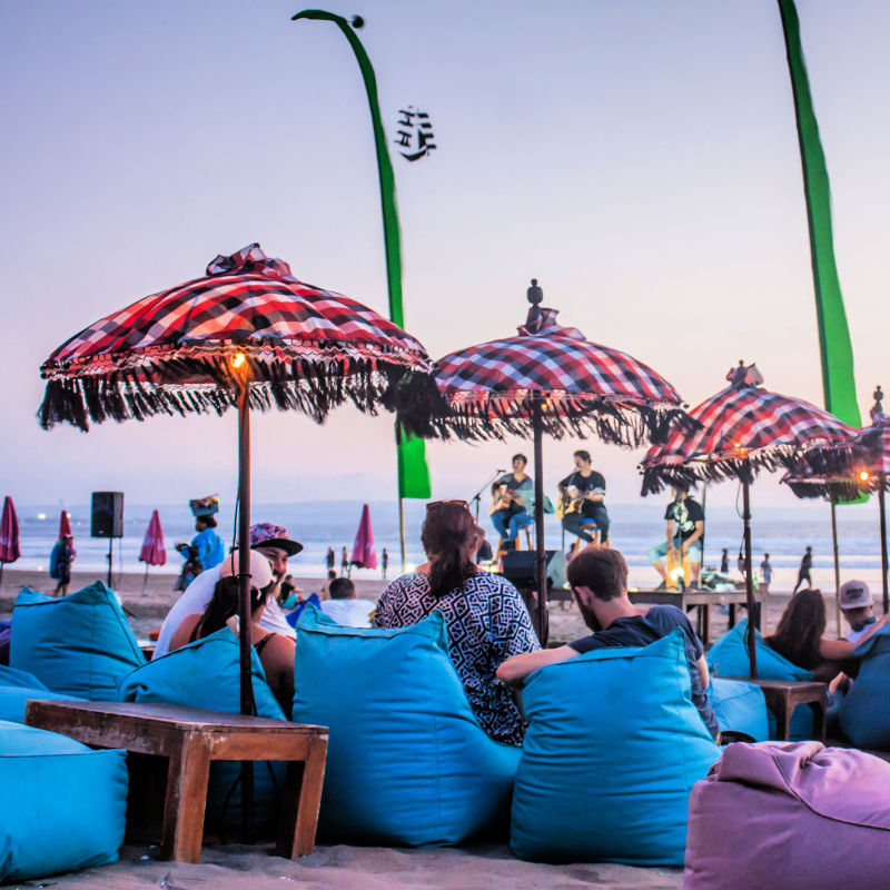 Tourists sit on blue and purple bean. bags at sunset on Bali beach