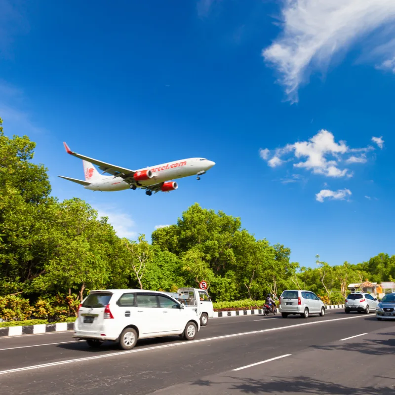Airplane-Begins-Descent-Into-Bali-Airport-Flying-Low-Over-Traffic-On-The-Road