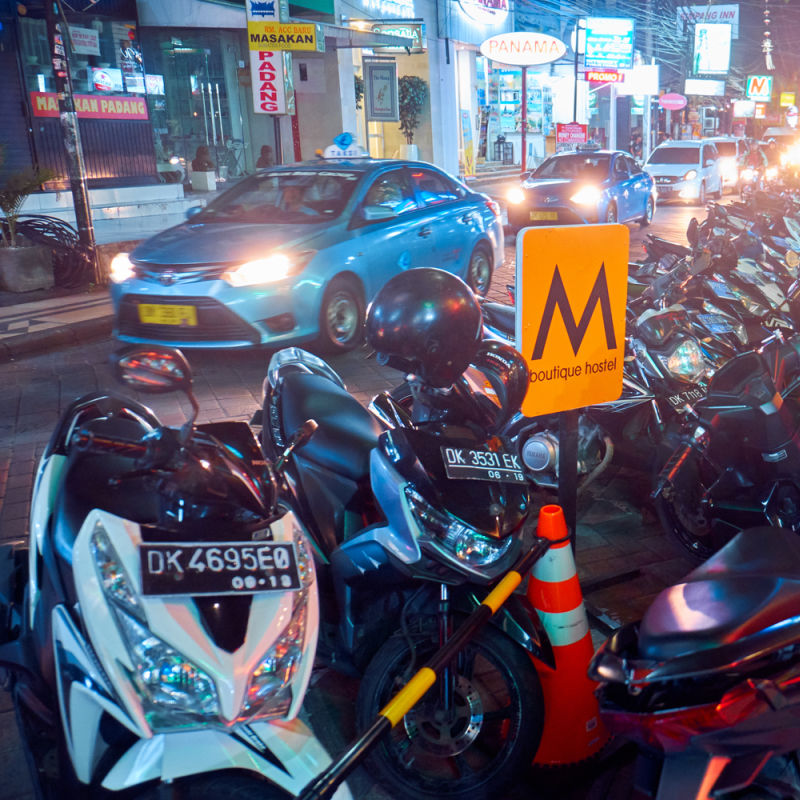 Mopeds And Taxi Cars Line Up On Busy Kuta Bali Street At Night