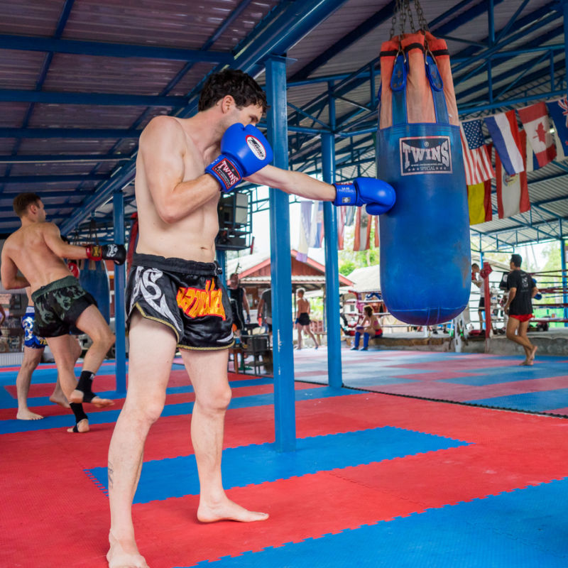 Sports Tourist Punches Boxing Bag In Gym In South East Asia While Training For MMA Or Muay Thai