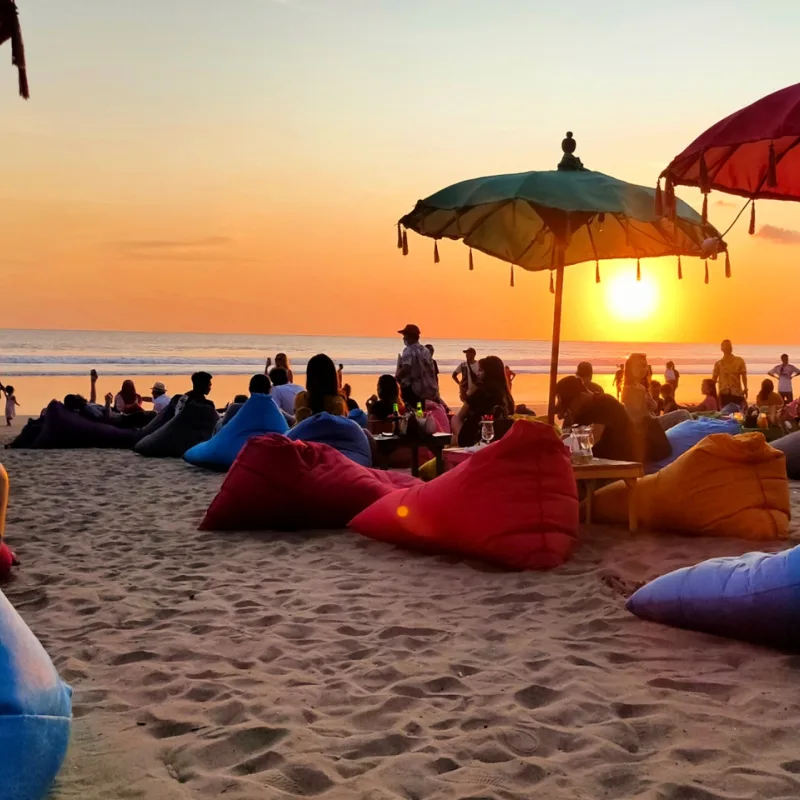 Tourists-On-Kuta-Beach-Enjoy-Sunset-From-Sun-Loungers-Under-Colourful-Umbrellas