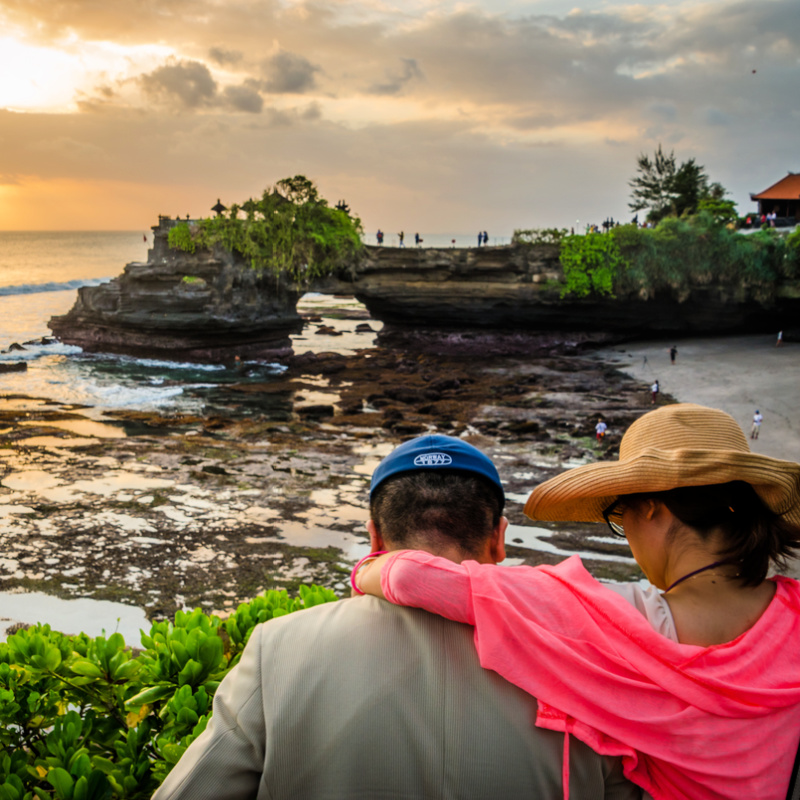 Two Tourists Man And Woman Look Over To Tanah Lot Temple In Bali At Sunset