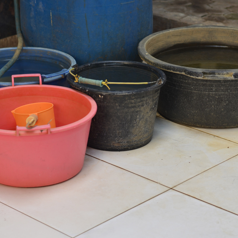 Water buckets stand on white tile floor in a home in Indonesia