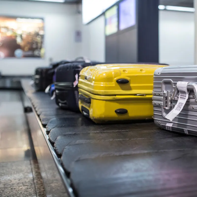 Yellow Suitcase Next To Other Darker Suits Cases on Luggage Carousel In Airport Arrivals Hall.