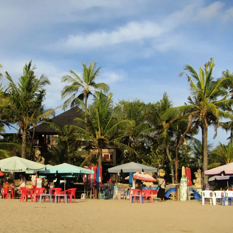 Beach-Bar-On-Kuta-Beach-Under-Palm-Trees-And-Sun-Umbrellas