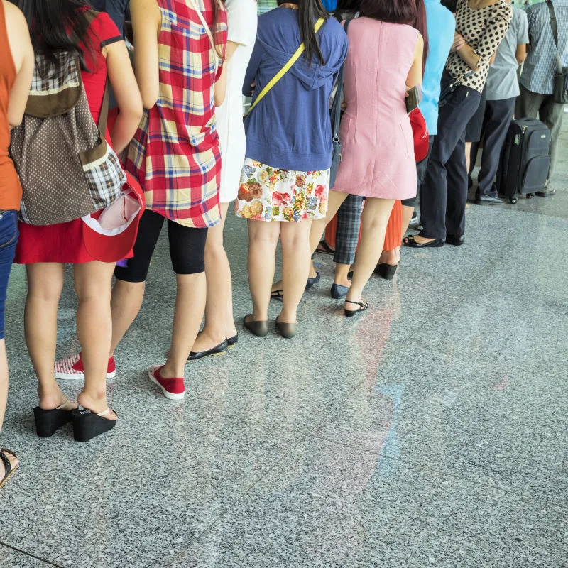 Close Up Of People Standing In A Queue On Grey Tiled Floor.