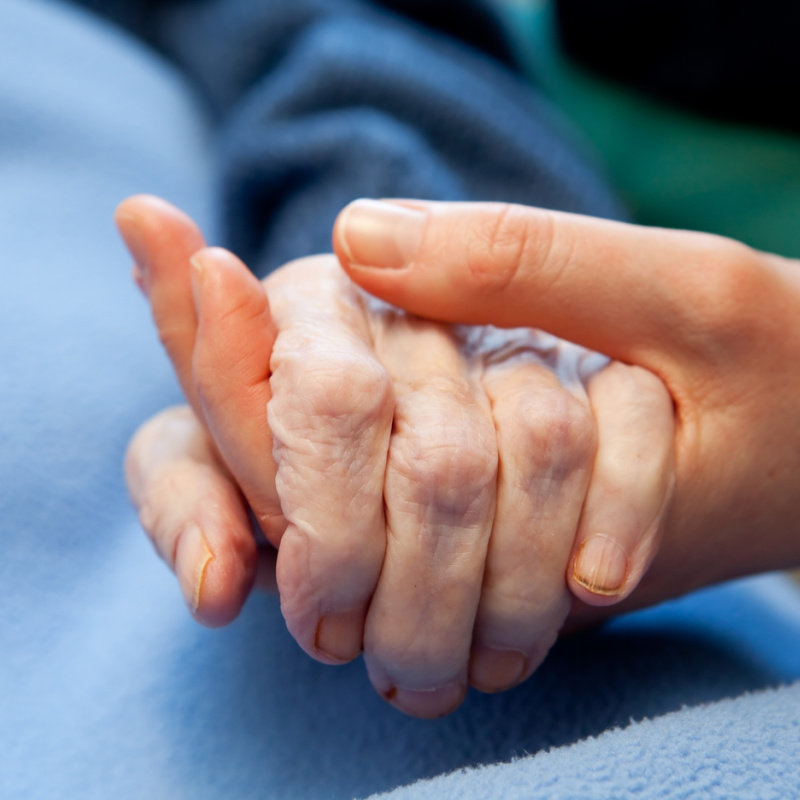 Close Up Of Young Hands Holding Old Hands In Hospital