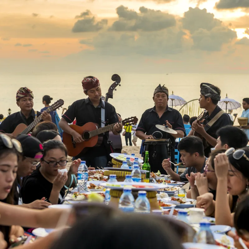 Domestic Tourists Enjoy Dinner On Bali Beach While Band Plays Music At The Table