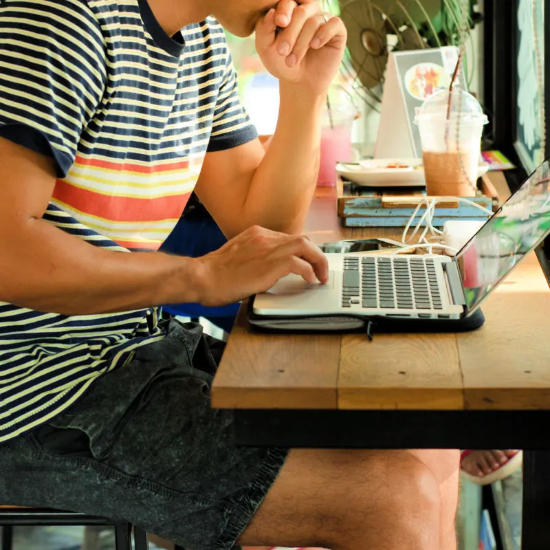 Man-In-A-Striped-Tshirt-works-on-his-laptop-at-a-cafe-in-Bali-as-a-digital-nomad