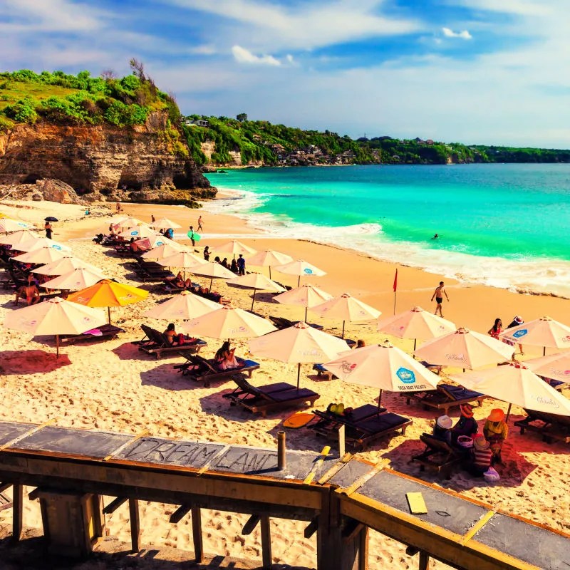 Tourist Relax under Umbrellas On Sun Loungers At Southern Bali Beach