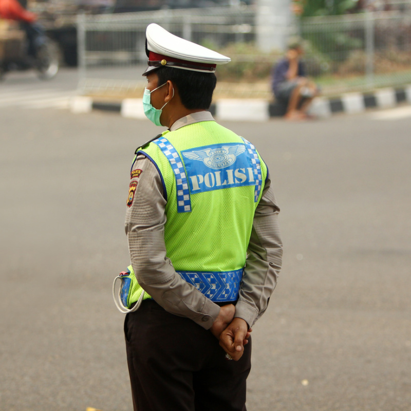 Traffic Police Officer In Bali Stands At The Side Of A Road
