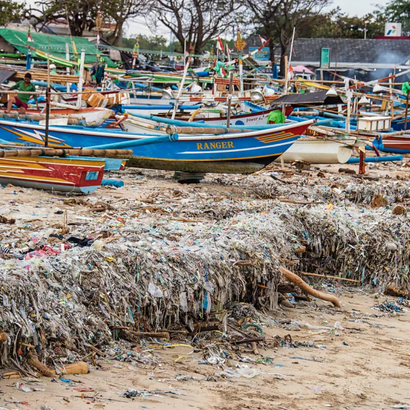 Bali Boats Docked On Beach Sit On Piles Of Plastic Waste And Ocean Garbage