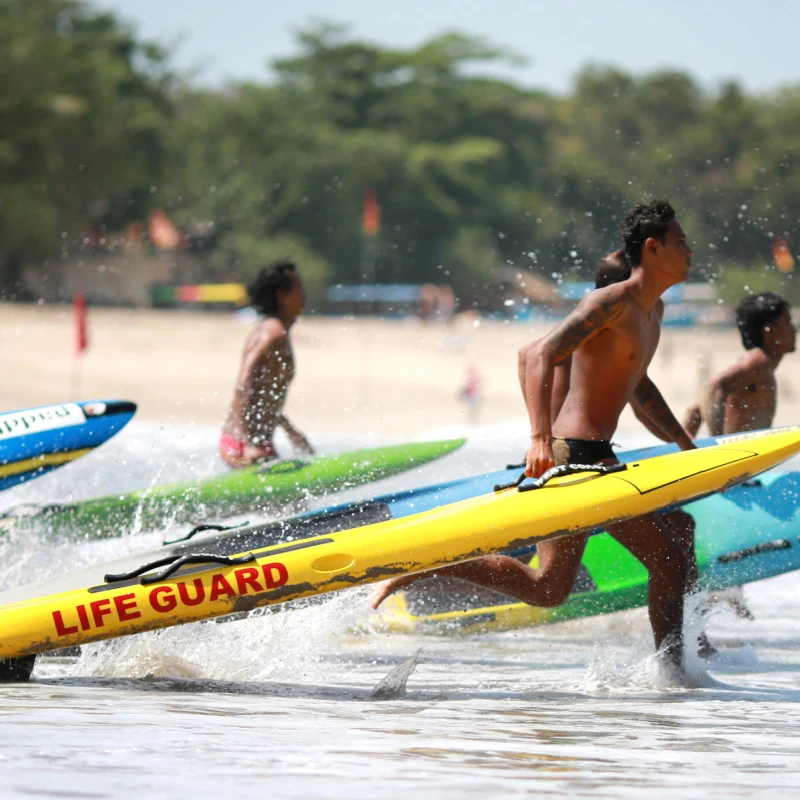 Bali Lifeguards Run Into The Sea Carrying Surfboards At Bali Beach.