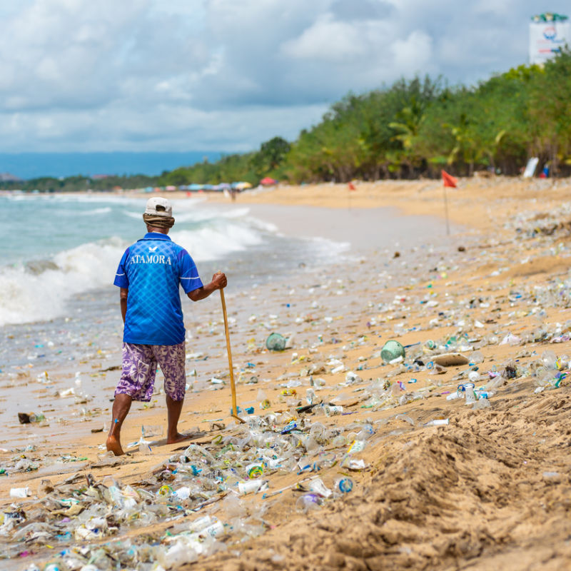 Indoneisan-Man-Walks-Along-Kuta-Beach-Covered-In-Plastic-Waste-And-Ocean-Garbage