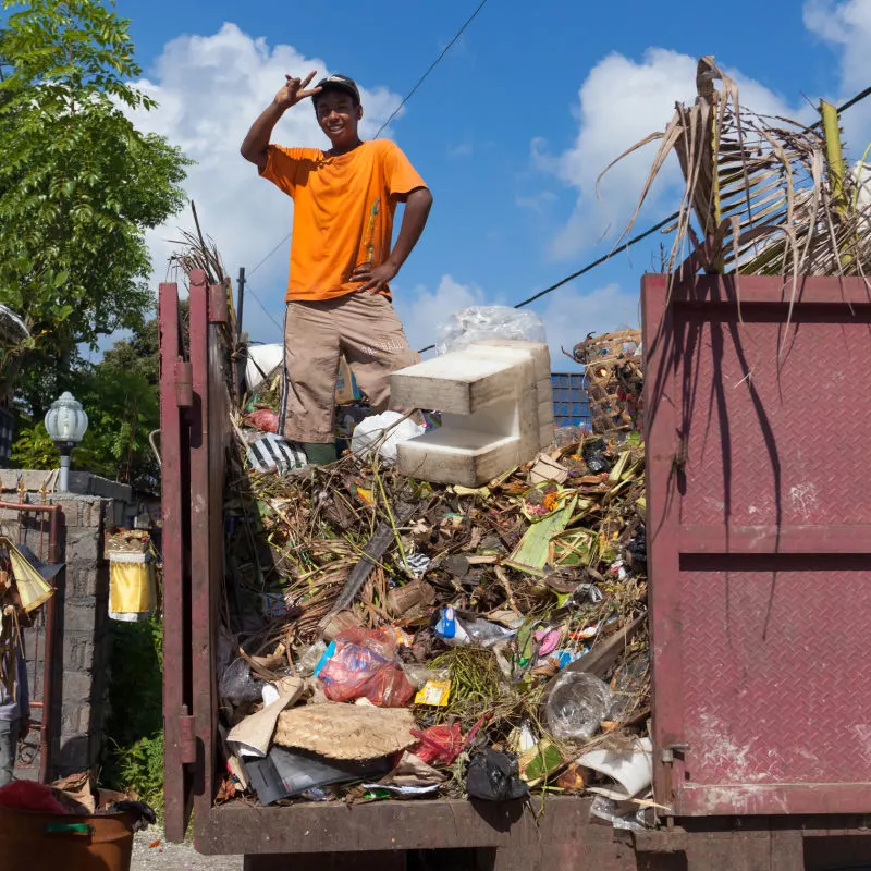 Man In Organe T-Shirt Stand In BAck Of Waste Collection Truck In Bali