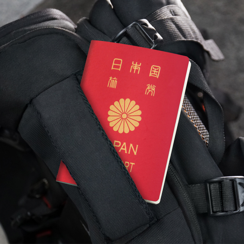 Red Japanese Passport Tucked Into The Handle Of A Black Backpack