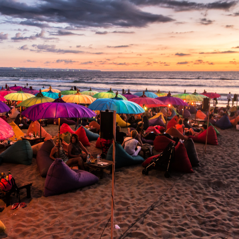 Sunset On Bali Beach Tourists Relax Under Colourful Umbrellas.