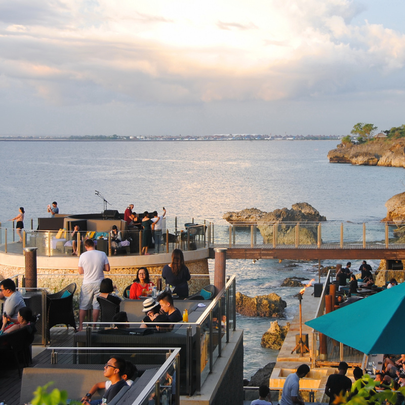 Tourists Enjoy Cliff Top Restaurant In Bali Over Ocean