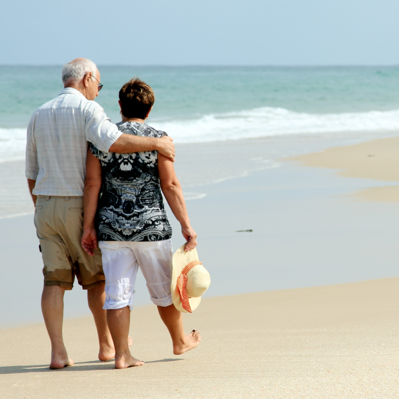 Old Retired Couple Walk Along The Beach