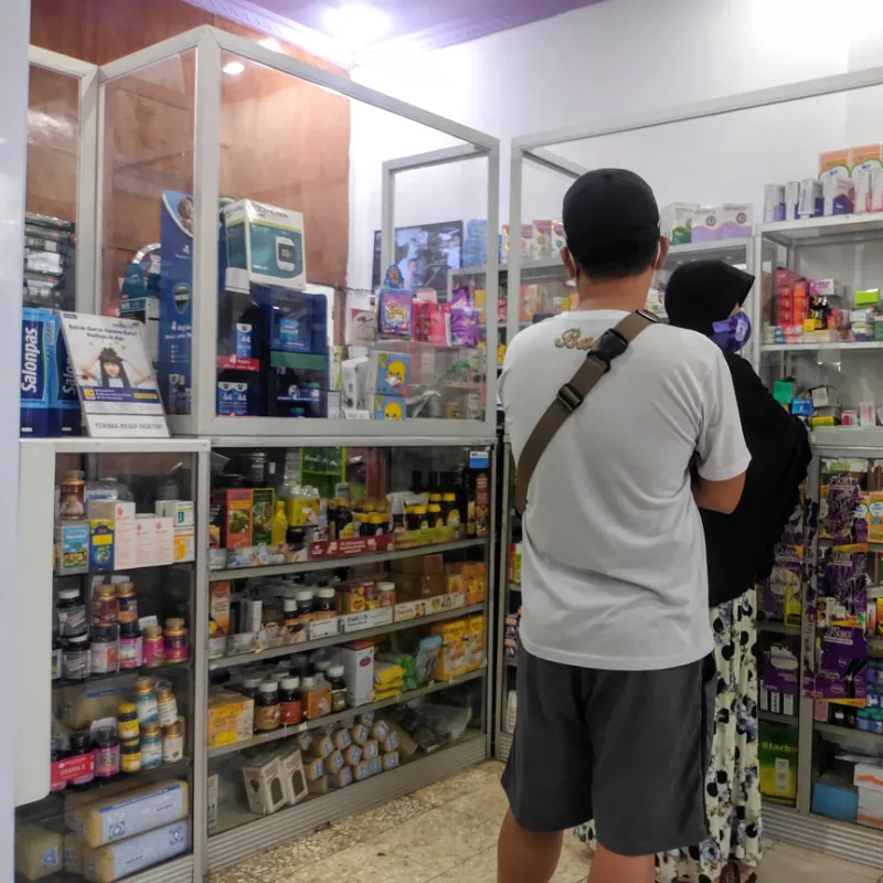 Two People Stand In Line At Bali Pharmacy