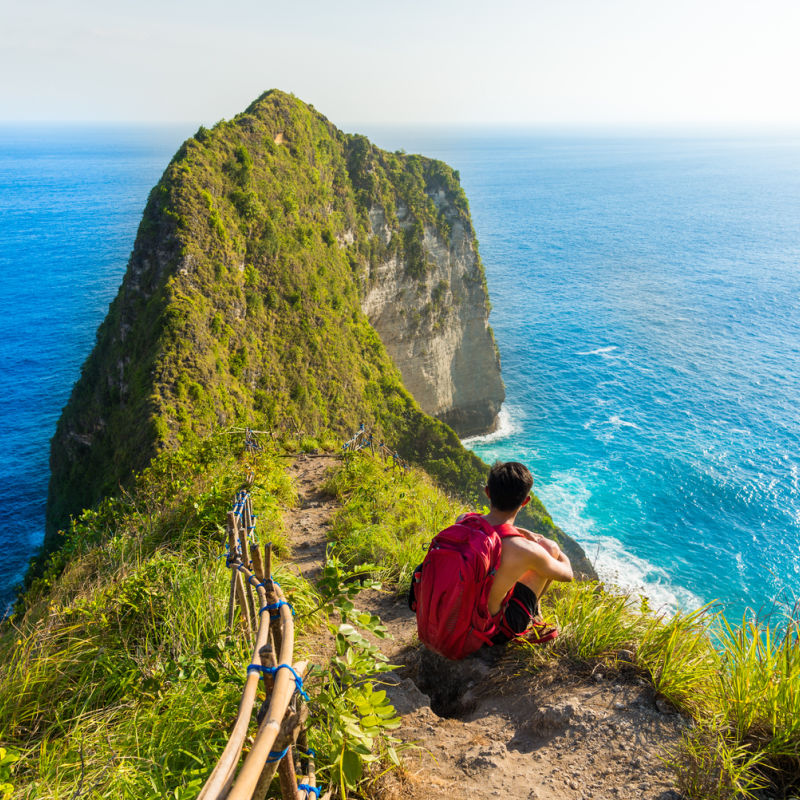 Tourist Crouches Down At the Top Of the Cliff At Kelingking Beach in Nusa Penida Bali