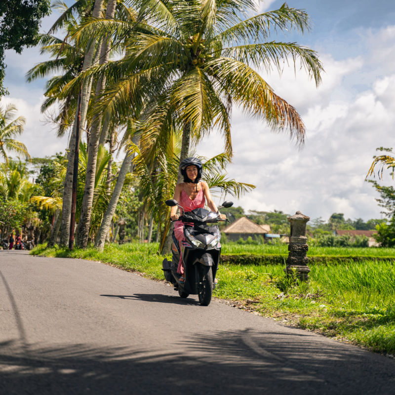 Woman Tourist Drives Moped In Rural Bali.