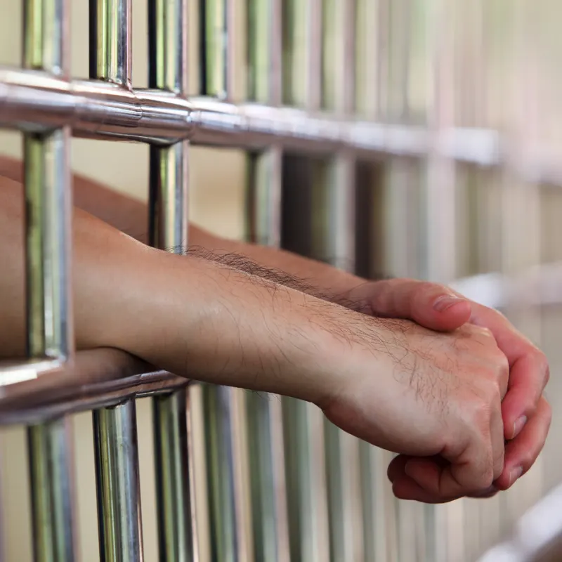 Close up of Criminal's arms and hands through a jail prison cell gate