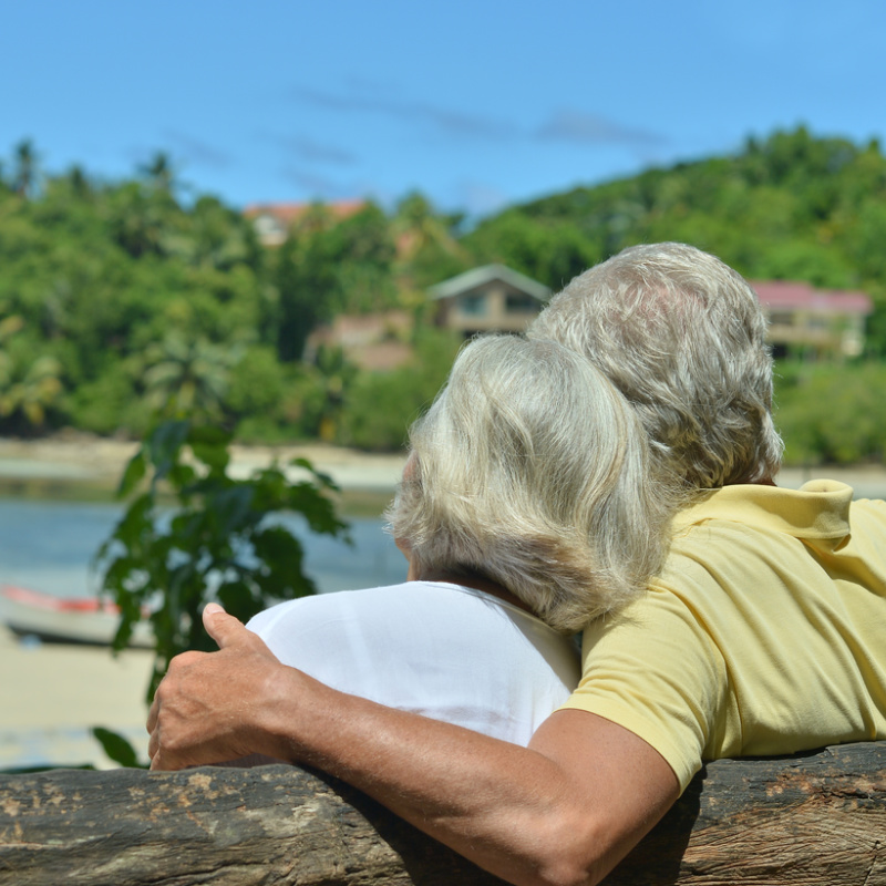 Old Eldery Couple Sit On Beach Looking At Ocean.jpg
