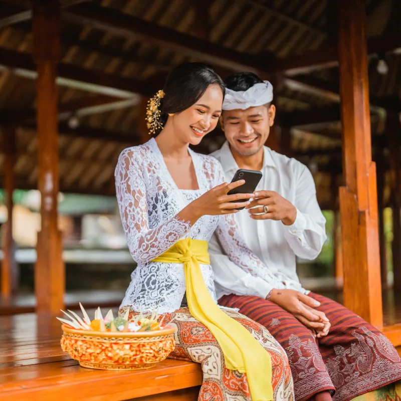 Pasangan muda Bali dengan pakaian tradisional menonton di ponsel