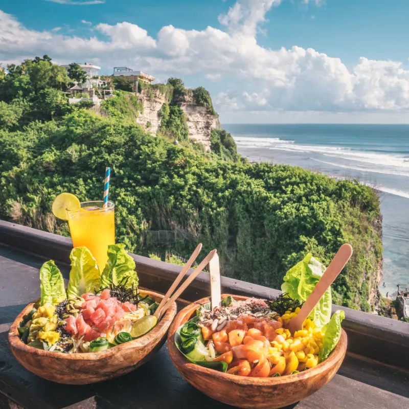 Fresh healthy salads with orange juice with an amazing view over the ocean and rocks in Uluwatu, Bali, Indonesia. Healthy food concept