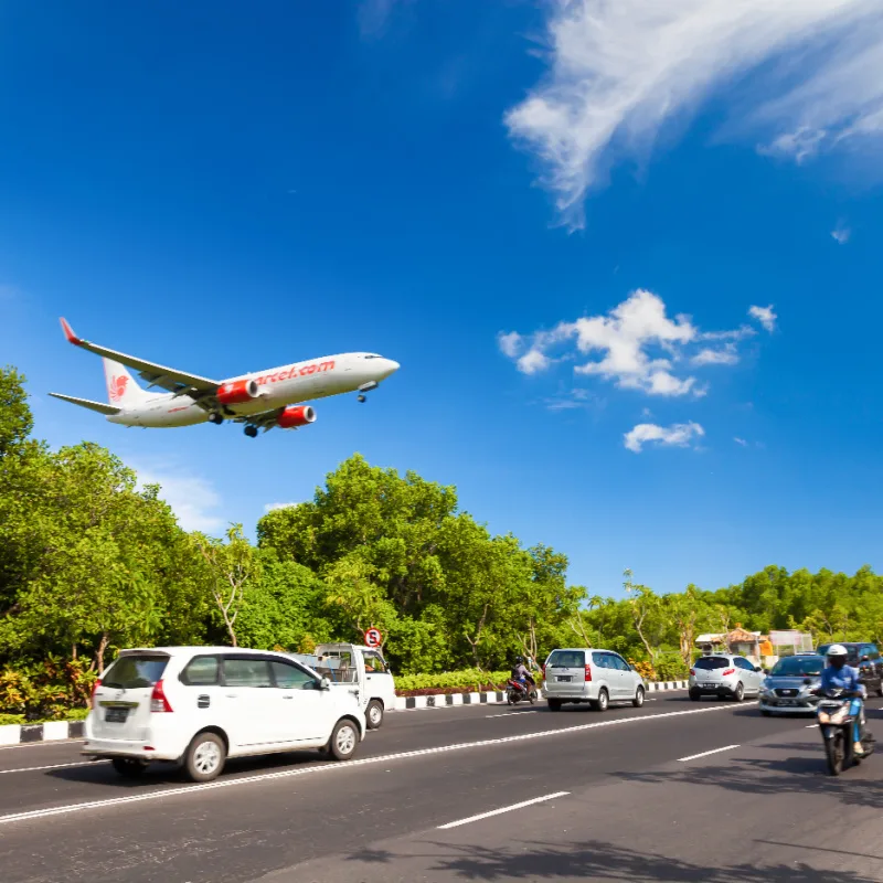 Airplane-coming-into-land-at-Bali-Airport-flies-over-cars-on-road-in-daytime