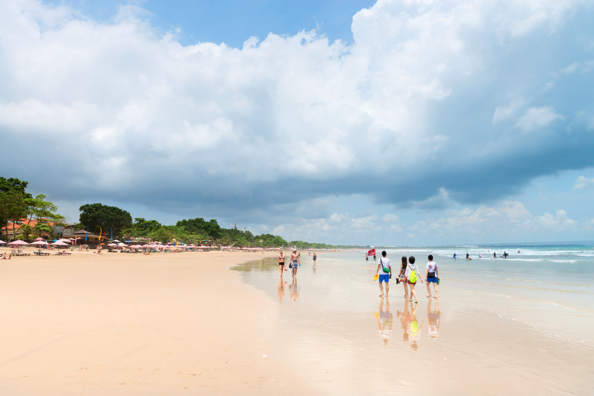 Tourists Walk Along Seminyak Beach in Bali At Low Tide In The Day Time
